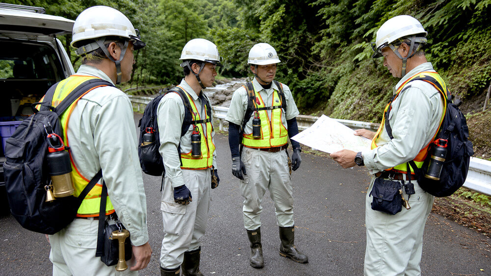 山間部の作業現場で熊よけ鈴とスプレーを携行する作業員