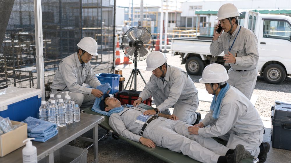 体調不良者を涼しい場所へ移し身体冷却と救急対応の手順を取る現場の様子